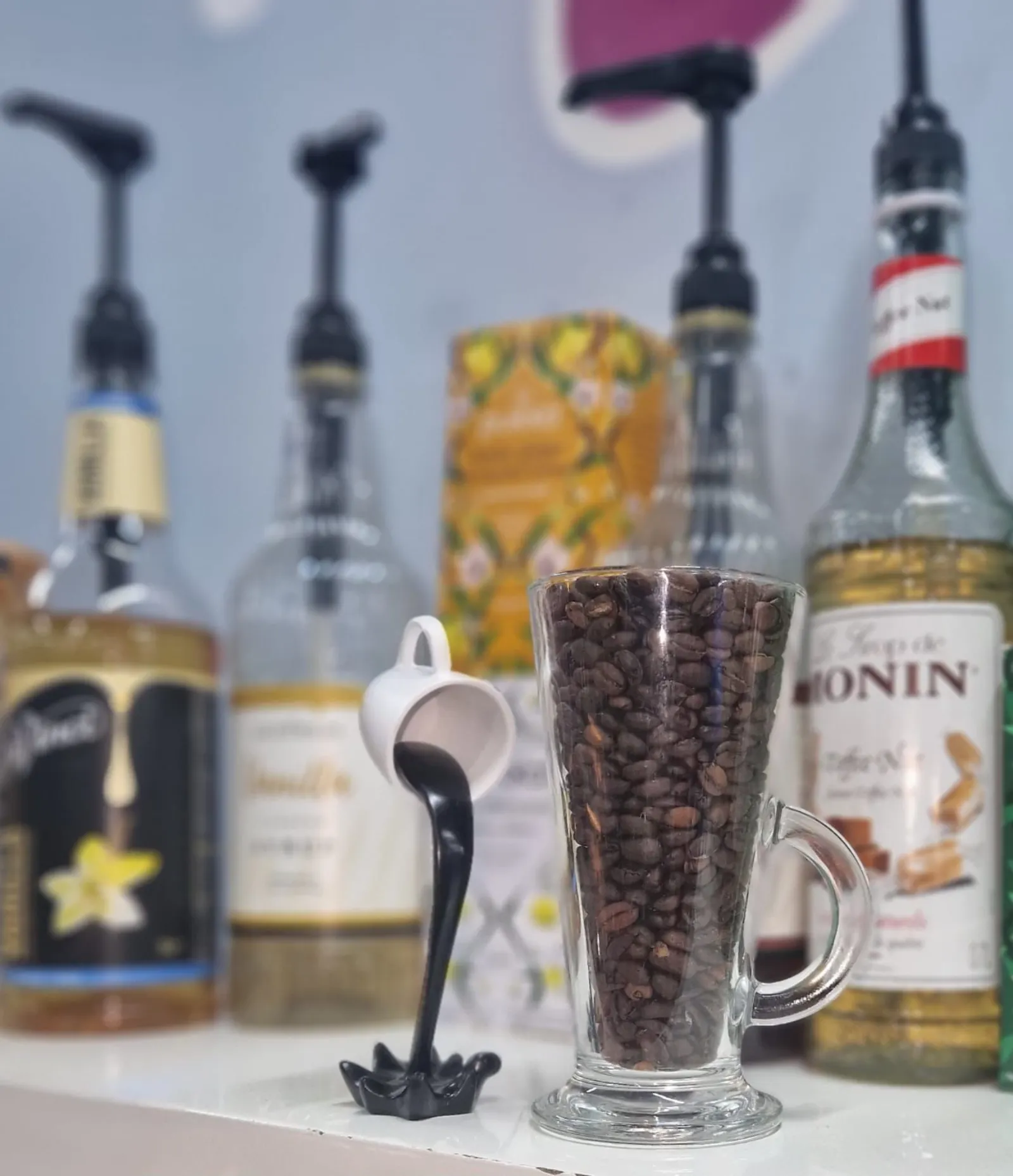 A glass of coffee beans beside a row of flavoured syrup bottles