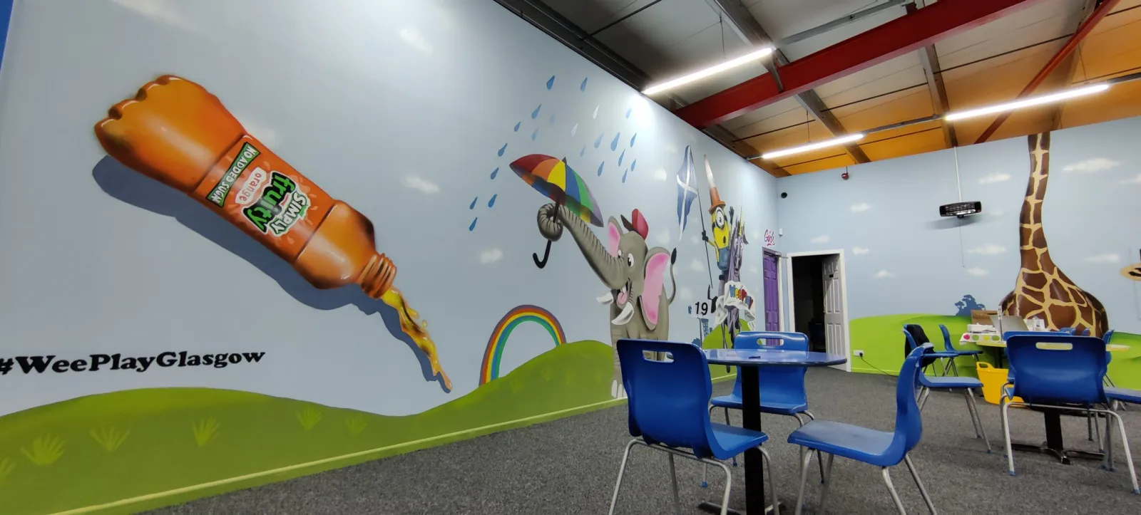 The WeePlay café seating area with a giraffe and rainbow mural